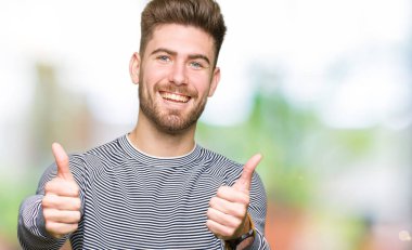 Çizgili süveter onaylama giyen genç yakışıklı adam el ile pozitif jest yapıyor gülümseyen ve başarı için mutlu yaşasın. Kamera, kazanan jest arıyorsunuz.