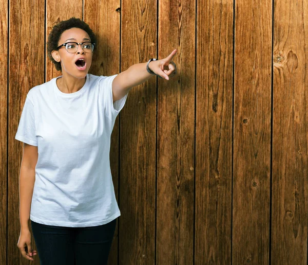 Güzel genç Afro-Amerikan kadın üzerinde gözlük takan izole arka plan ile sürpriz devam parmakla, açık ağız hayret ifadesi, önünde bir şey