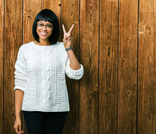 Güzel genç Afro-Amerikan kadın gözlük gösterilen ve parmakları ile işaret izole arka plan üzerinde kendinden emin ve mutlu gülümseyerek iken ikincisi.