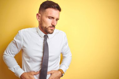 Genç yakışıklı iş adamı mide üzerinde el ile sarı izole arka plan üzerinde zarif beyaz gömlek giyen çünkü mide bulantısı, ağrılı hastalık kötü hissediyorum. Ağrı kavramı.