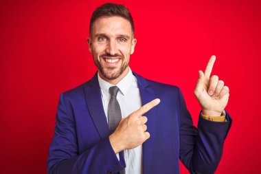 Kırmızı izole arka plan üzerinde genç yakışıklı iş adamı gülümseyerek ve yan iki el ve parmakları ile işaret kamera bakıyor.