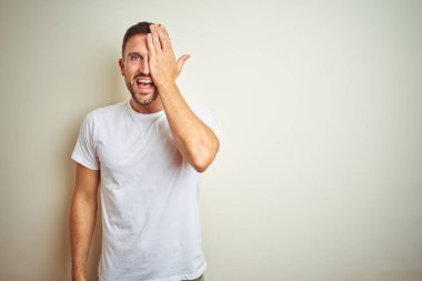 Genç yakışıklı adam izole arka plan üzerinde rahat beyaz t-shirt giyen el, yüz ve sürpriz duygu üzerinde kendine güvenen gülümseme ile bir göz kapsayan.