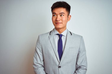 Asian chinese businessman wearing grey jacket and tie standing over isolated white background smiling looking to the side and staring away thinking.