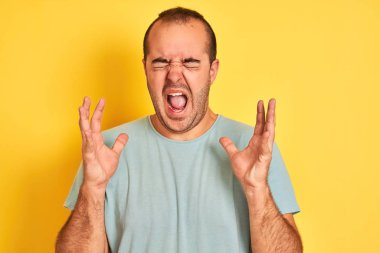 Yeşil günlük tişört giyen genç adam, izole edilmiş sarı arka planda duruyor. Kolları havada ve gözleri kapalı heyecanla haykırarak başarının çılgınlığını kutluyor. Kazanan konsept