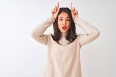 Balıkçı yaka kazak giyen güzel Çinli kadın izole edilmiş beyaz arka planda dikiliyor ve boynuzlarını başlarının üzerinde gezdirerek komik hareketler yapıyor.