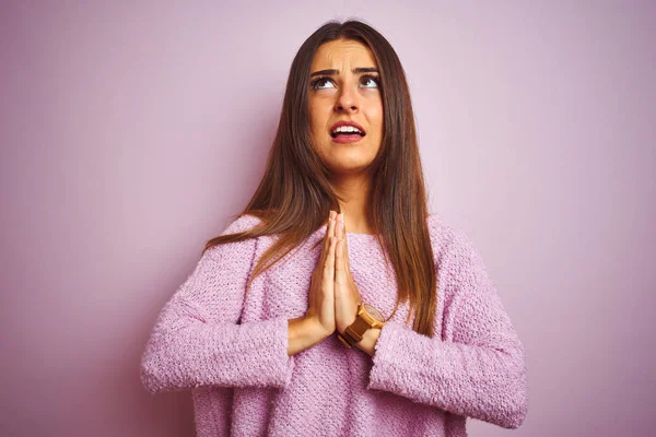 Young beautiful woman wearing casual sweater standing over isolated pink background begging and praying with hands together with hope expression on face very emotional and worried. Asking for forgiveness. Religion concept.