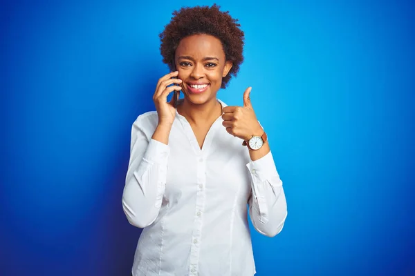 青い孤立した背景の上にスマートフォンで話すアフリカ系アメリカ人女性は Okサインをやって大きな笑顔で幸せ 指で親指アップ 優れた兆候 — ストック写真