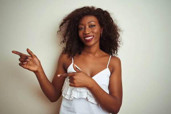 Tシャツを着た若いアフリカ系アメリカ人の女性が白い背景の上に立って笑っていて カメラを見て両手と指で側面を指差している — ストック写真