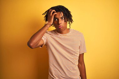 Izole sarı arka plan üzerinde duran çizgili t-shirt giyen dreadlocks ile Afro adam endişeli ve alnında el ile ilgili bir sorun hakkında vurguladı, sinir ve kriz için endişeli