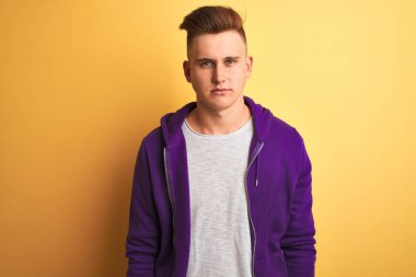 Mor sweatshirt giyen genç yakışıklı adam izole sarı arka plan üzerinde duran yüzünde ciddi ifade ile rahat. Kameraya basit ve doğal bir bakış.