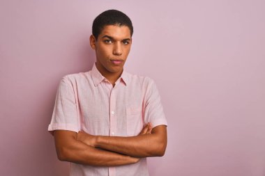 İzole edilmiş pembe arka plan üzerinde duran rahat gömlekli genç, yakışıklı Arap adam şüpheci ve gergin, yüzünde çapraz kollu tasvip etmeyen ifade. Negatif kişi.