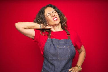 Kırmızı izole arka plan üzerinde önlük giyen orta yaş yaşlı kadın Boyun ağrısı yaralanması acı, el ile boyun dokunmadan, kas ağrısı