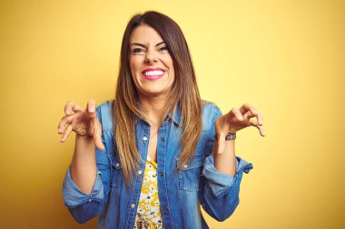 Sarı arka planda duran genç ve güzel bir kadın komik bir şekilde gülüyor kedi gibi pençe hareketi yapıyor, agresif ve seksi bir ifade.