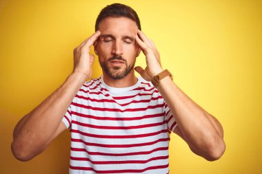 Genç yakışıklı adam sarı izole arka plan üzerinde rahat kırmızı çizgili t-shirt giyen baş ağrısı için el ile stres çünkü. Acı çeken migren.