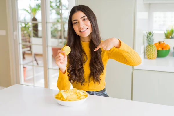 若いです女性食べるファーストフードポテトチップスとともに驚きの顔を指差す指彼自身 — ストック写真