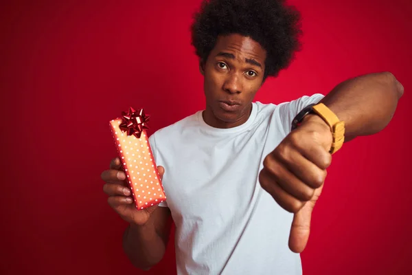 年轻的非洲裔美国男子拿着情人节礼物站在孤立的红色背景与愤怒的脸 负面的标志显示不喜欢与拇指向下 拒绝概念 — 图库照片