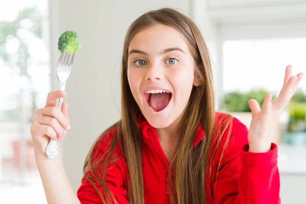 新鮮なブロッコリーを食べる美しい若い女の子は非常に幸せで興奮し 大きな笑顔で叫んで勝利を祝う勝者の表情と手を上げた — ストック写真