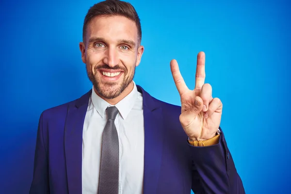 Close up picture of young handsome business man over blue isolated background smiling with happy face winking at the camera doing victory sign. Number two.