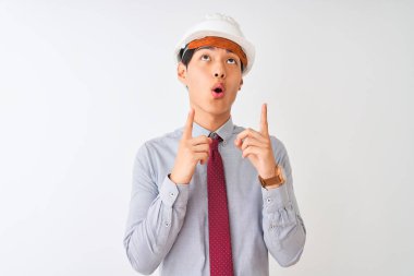 Izole beyaz arka plan üzerinde duran kravat ve kask giyen Çinli mimar adam şaşırttı ve yukarı bakarak ve parmakları ile işaret ve kolları kaldırdı şaşırttı.