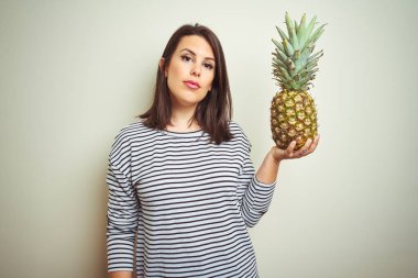 Genç güzel kadın ciddi düşünme akıllı yüz üzerinde emin bir ifade ile izole arka plan üzerinde tropikal meyve ananas tutan