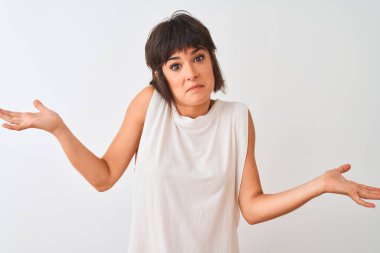 Genç güzel kadın rahat t-shirt izole beyaz arka plan üzerinde duran giyen habersiz ve kolları ve elleri ile karışık ifade kaldırdı. Şüphe kavramı.