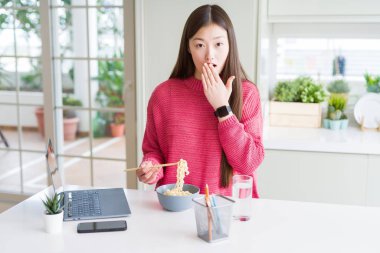 Güzel Asyalı kadın laptop kullanarak çalışan ve Asya noodle yeme el ile hata, korku ifade, sessizlik, gizli kavramı korkuyor ifadesi utanç ile şok ağzını kapak