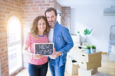Orta yaş Senior çift yeni bir eve hareket, yeni bir ev metin ile bir tahta tutan Apartmant aşık mutlu gülümseyen