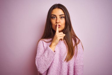 Genç güzel kadın rahat kazak giyen izole pembe arka plan üzerinde dudaklarında parmak ile sessiz olmak isteyen ayakta. Sessizlik ve gizli kavram.