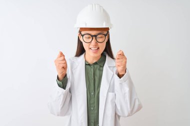 İzole beyaz arka plan üzerinde palto kask gözlük takan genç Çinli mühendis kadın kollarını kaldırdı ve gözleri gülümseyerek zafer kutluyor kapalı başarı için heyecanlı. Kazanan kavramı.