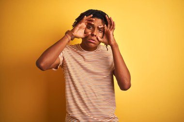 İzole sarı arka plan üzerinde duran çizgili t-shirt giyen dreadlocks ile Afro adam parmakları ile gözleri açmaya çalışıyorum, uykulu ve sabah yorgunluğu için yorgun