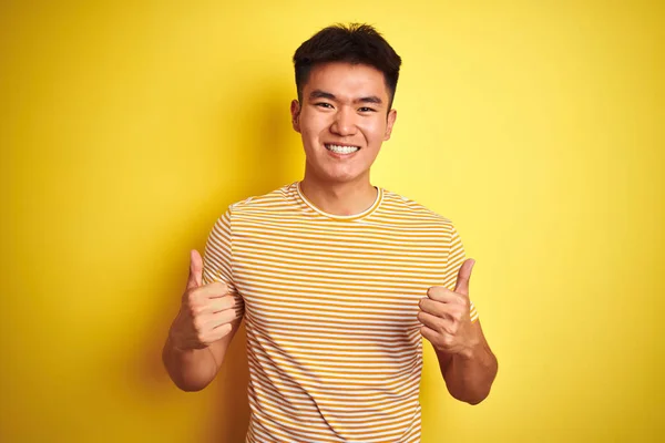 年轻的亚洲中国男子穿着T恤站在孤立的黄色背景成功标志做积极的姿态与手 竖起大拇指微笑和快乐 欢快的表情和获胜的手势 — 图库照片