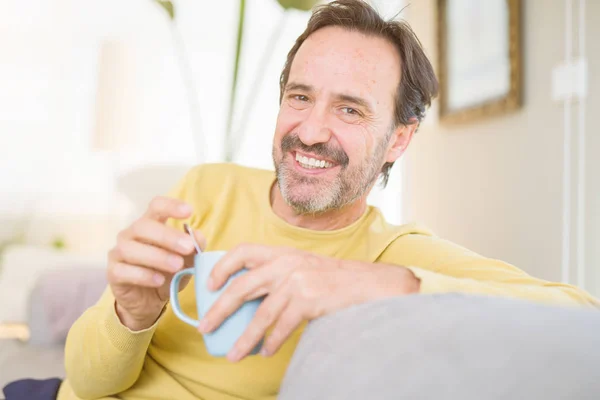 ハンサムな中年男がソファーに座ってリラックス コーヒーを一杯飲み 自宅のカメラで笑顔 — ストック写真