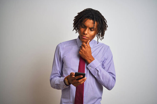 Afro american businessman with dreadlocks using smartphone over isolated white background serious face thinking about question, very confused idea