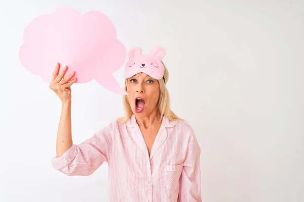 Middle age woman wearing sleep mask holding speech bubble over isolated white background scared in shock with a surprise face, afraid and excited with fear expression