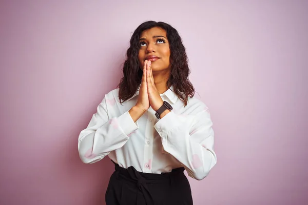 Transsexual transgender businesswoman standing over isolated pink background begging and praying with hands together with hope expression on face very emotional and worried. Asking for forgiveness. Religion concept.