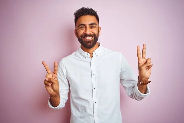 孤立したピンクの背景の上に立つエレガントなシャツを着た若いインド人ビジネスマンは 勝利のサインをしている指を示すカメラに微笑みかけています ナンバー2 — ストック写真