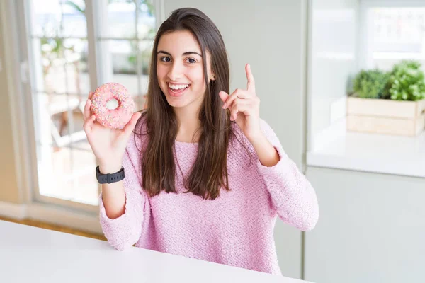 ピンクのチョコチップを食べる美しい若い女性ドーナツは 幸せな顔で指を指すアイデアや質問に驚きました ナンバーワン — ストック写真