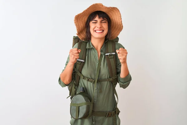 Hiker woman wearing backpack hat and water canteen over isolated white background excited for success with arms raised and eyes closed celebrating victory smiling. Winner concept.
