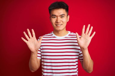 Genç asyalı Çinli adam çizgili t-shirt izole kırmızı arka plan üzerinde duran gösteren ve parmakları ile işaret ederken emin ve mutlu gülümseyerek on numara.