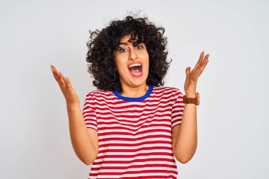 Kıvırcık saçlı genç arap kadın izole beyaz arka plan üzerinde çizgili t-shirt giyen deli kutluyor ve kollarını kaldırdı ve açık gözleri ile başarı için hayran heyecanlı çığlık. Kazanan kavramı