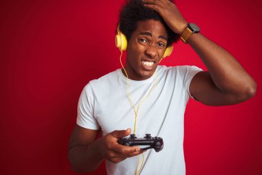 Afro oyun adam izole kırmızı arka plan üzerinde joystick kulaklık kullanarak video oyunu oynarken baş el ile vurguladı, utanç ve sürpriz yüz ile şok, kızgın ve sinirli. Korku ve hata için üzgün.
