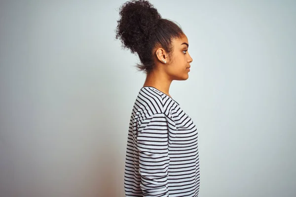 African american woman wearing navy striped t-shirt standing over isolated white background looking to side, relax profile pose with natural face and confident smile.