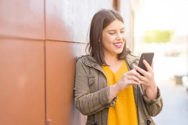 Krásná Mladá Žena Pozitivně Usmívá Pomocí Smarpthone Který Opírá Zeď — Stock fotografie