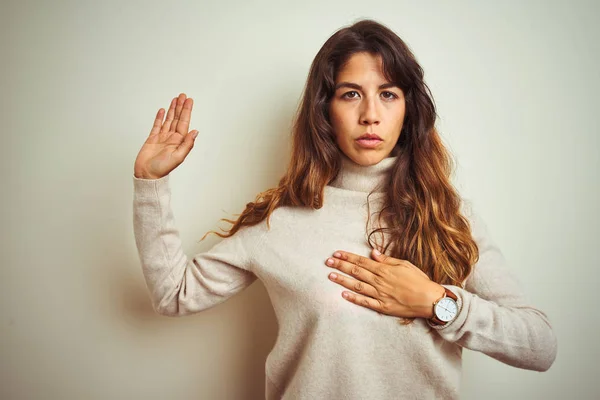Young beautiful woman wearing winter sweater standing over white isolated background Swearing with hand on chest and open palm, making a loyalty promise oath