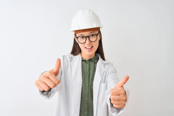 孤立した白い背景の上にコートヘルメットのメガネをかけた若い中国人エンジニアの女性は 手で肯定的なジェスチャーを行い 親指を笑顔で成功に喜びました 勝者のジェスチャー — ストック写真