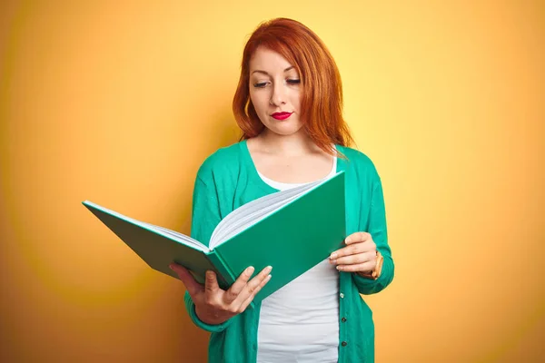 Молодая Рыжая Студентка Читает Зеленую Книгу Желтом Изолированном Фоне Уверенным — стоковое фото