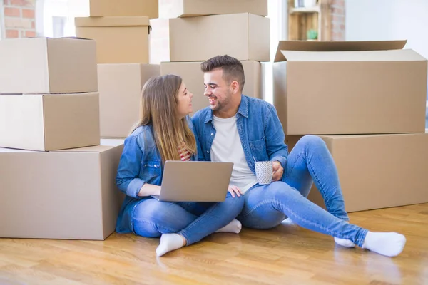 Pareja joven sentada en el suelo alrededor de cajas de cartón usando c — Foto de Stock