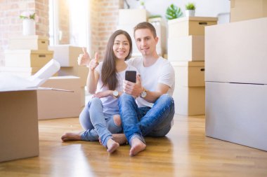 Güzel bir çift yeni evinde, karton kutuların etrafında akıllı telefon kullanıyor. Gülümsüyor ve gülümsüyor. İşaret veriyor.