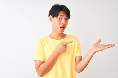 Izole beyaz arka plan üzerinde duran sarı rahat t-shirt giyen Çinli adam şaşırttı ve el ile sunarken kameraya gülümseyerek ve parmak ile işaret.
