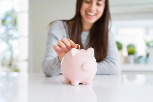 Mujer joven sonriendo poniendo una moneda dentro de alcancía como ahorros — Foto de Stock